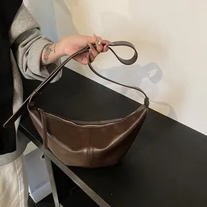 Detalle de un bolso de media luna marrón oscuro con cuero PU brillante y cierre de cremallera