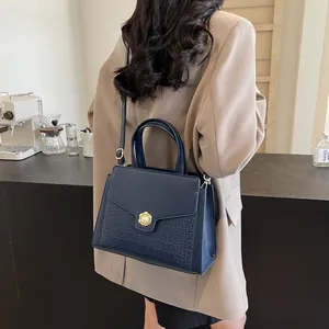 Detail of dark blue tote with crocodile texture and golden pearl buckle on a model