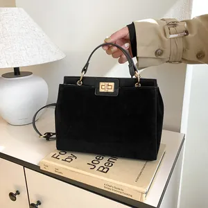 Gros plan du sac Kelly en daim noir avec fermoir tournant doré et cuir lisse