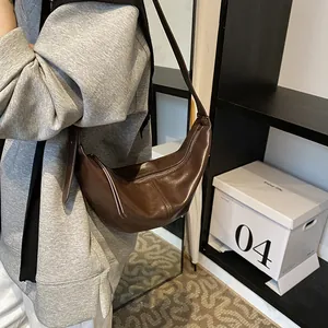 Detalle del bolso de media luna en cuero sintético marrón oscuro colgado al hombro