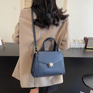 Navy blue faux crocodile leather handbag worn as a crossbody bag by a female model