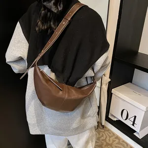 Detalle de un bolso bandolera de cuero marrón en forma de media luna con correa ajustable