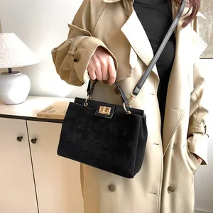 Détail du sac Kelly en daim noir avec fermoir doré et bandoulière sur trench-coat