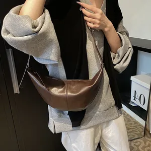 Detalle de un bolso bandolera de media luna marrón oscuro con acabado de cuero mate liso