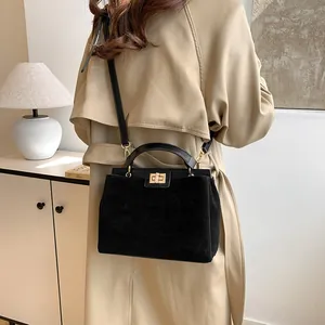 Détail du sac Kelly noir en daim avec fermoir doré dans un décor lifestyle élégant