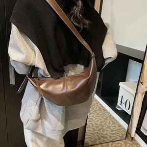 Detalle del bolso de media luna en cuero marrón oscuro con correa ajustable en modelo