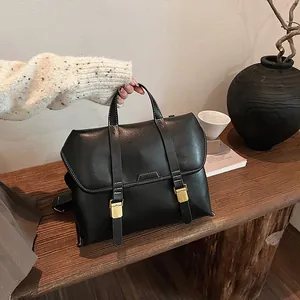 Detail of black leather briefcase bag with white contrast stitching and gold buckles
