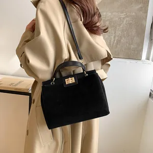 Femme en trench-coat kaki portant un sac Kelly en cuir noir mat avec fermoir doré