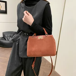 Sac Kelly trapèze en daim caramel avec fermoir rotatif doré porté par un mannequin