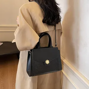 Detail of black croc-embossed handbag with elegant gold pearl buckle and smooth leather