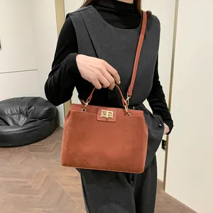 Détail d'un sac cabas en daim fauve avec boucle dorée porté par un mannequin