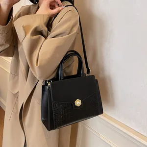 Detail of black faux leather tote with crocodile pattern and pearl clasp on trench coat