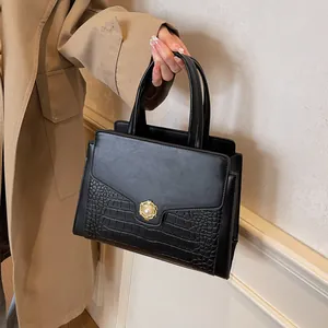 Close-up of black handbag featuring faux crocodile texture and pearl flower metal buckle