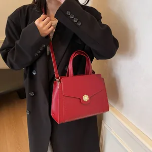 Detail of red croc-embossed tote bag featuring a gold floral pearl buckle and strap