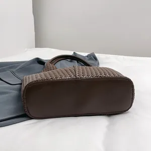 Detailed view of dark brown woven tote bag featuring textured PU leather and round handle