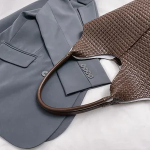 Close-up of a dark brown woven leather tote bag resting on a professional grey blazer