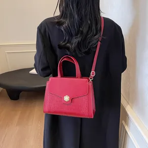 Detail of red croc-embossed tote bag featuring a gold floral pearl clasp and slim strap