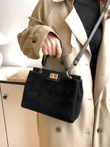 Sac Kelly en daim noir avec boucle dorée et bandoulière porté avec un trench-coat kaki