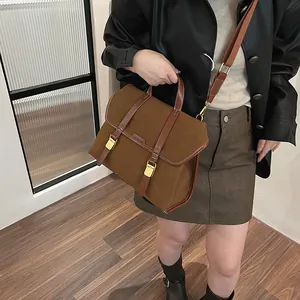 Close-up of caramel brown frosted suede messenger bag with gold buckles and wide strap