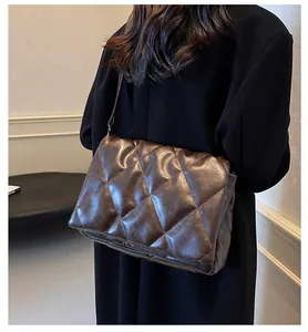 Détail d'un sac bandoulière marron matelassé en cuir souple porté par un mannequin