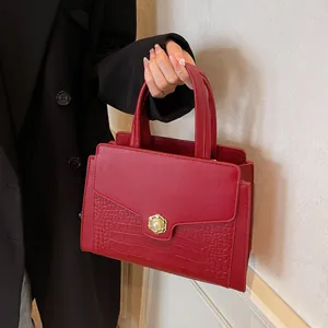 Detail of red croc-embossed tote bag featuring a gold floral pearl clasp and smooth top handle
