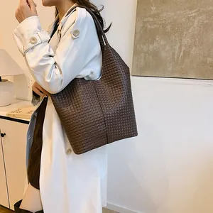 Detail of a dark brown woven tote bag worn on shoulder by a model in a minimalist setting