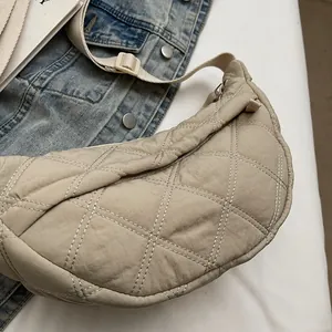 Detail of beige quilted crescent bag featuring adjustable strap and puffy nylon material