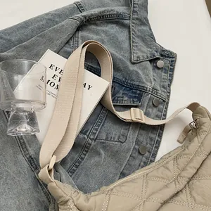 Close-up of beige quilted puffer crossbody bag with adjustable strap on denim jacket