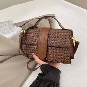 Detail of a deep brown woven texture handbag with leather strap and golden hardware