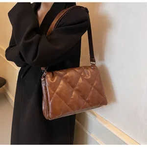Détail du sac bandoulière matelassé marron en similicuir brillant sur un manteau noir