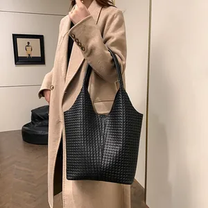 Detail of a large black woven tote bag with smooth leather handle on a beige coat