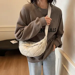 Close-up of off-white quilted crescent bag with wide strap and nylon texture detail