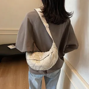 Quilted beige half-moon crossbody bag with adjustable wide strap on a female model