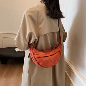 Close-up of orange quilted nylon crescent bag worn by a model in a khaki trench coat