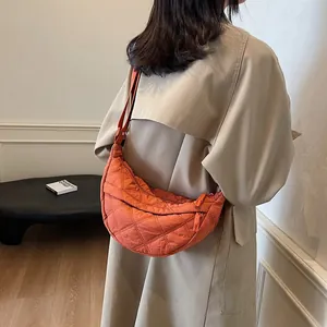 Detail of orange quilted crescent bag with adjustable strap worn with a khaki coat