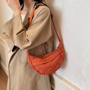 Detail of orange quilted crescent shoulder bag with diamond pattern on a female model