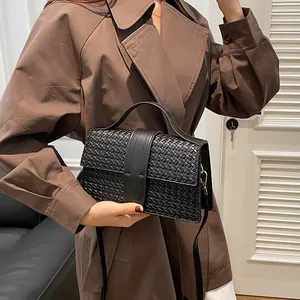 Detailed close-up of a black woven leather crossbody bag styled with a brown coat