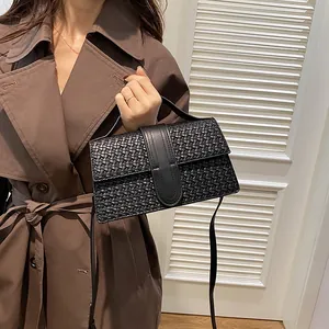 Detail of black woven crossbody bag shown with an elegant trench coat on a model