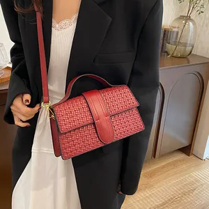 Detail of red woven leather handbag featuring gold hardware on a model with black blazer