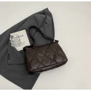 Détails matelassés d'un sac bandoulière marron foncé sur un blazer gris chic