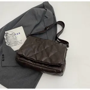 Détail d'un sac bandoulière marron foncé matelassé à losanges posé sur un blazer gris
