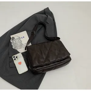 Sac bandoulière marron matelassé posé sur un blazer gris avec accessoires