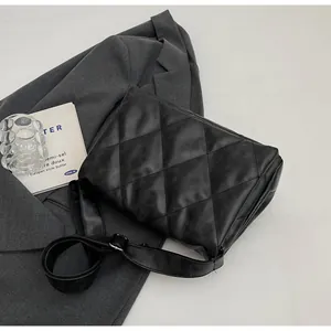 Détail du sac bandoulière noir matelassé avec surpiqûres sur un blazer gris