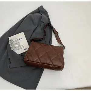 Détail du sac bandoulière marron en cuir PU matelassé sur une veste grise chic
