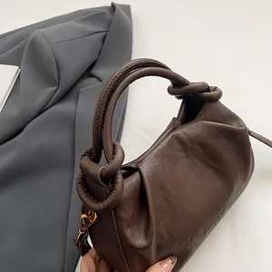 Detail of dark brown ruched cloud bag featuring knot handle and golden metal hooks