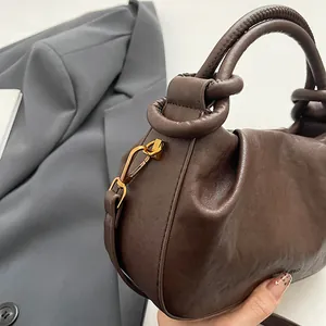 Detail of dark brown pleated cloud bag with knotted handle and gold metal hardware