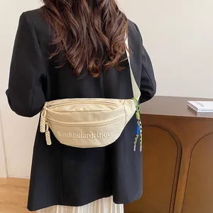 Detailaufnahme der cremeweißen Canvas-Brusttasche mit verstellbarem Gurt und Etikett