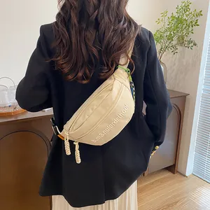 Detailaufnahme einer beige halbmondförmigen Brusttasche mit weißer Buchstabenstickerei