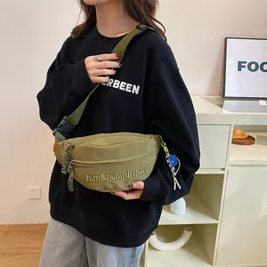 Nahaufnahme der olivgrünen Canvas-Brusttasche mit Stickerei und verstellbarem Gurt am Model