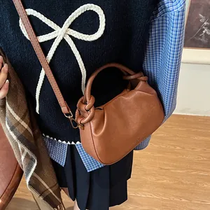 Detail of a brown leather pleated bag with a knotted handle and embossed fashion logo